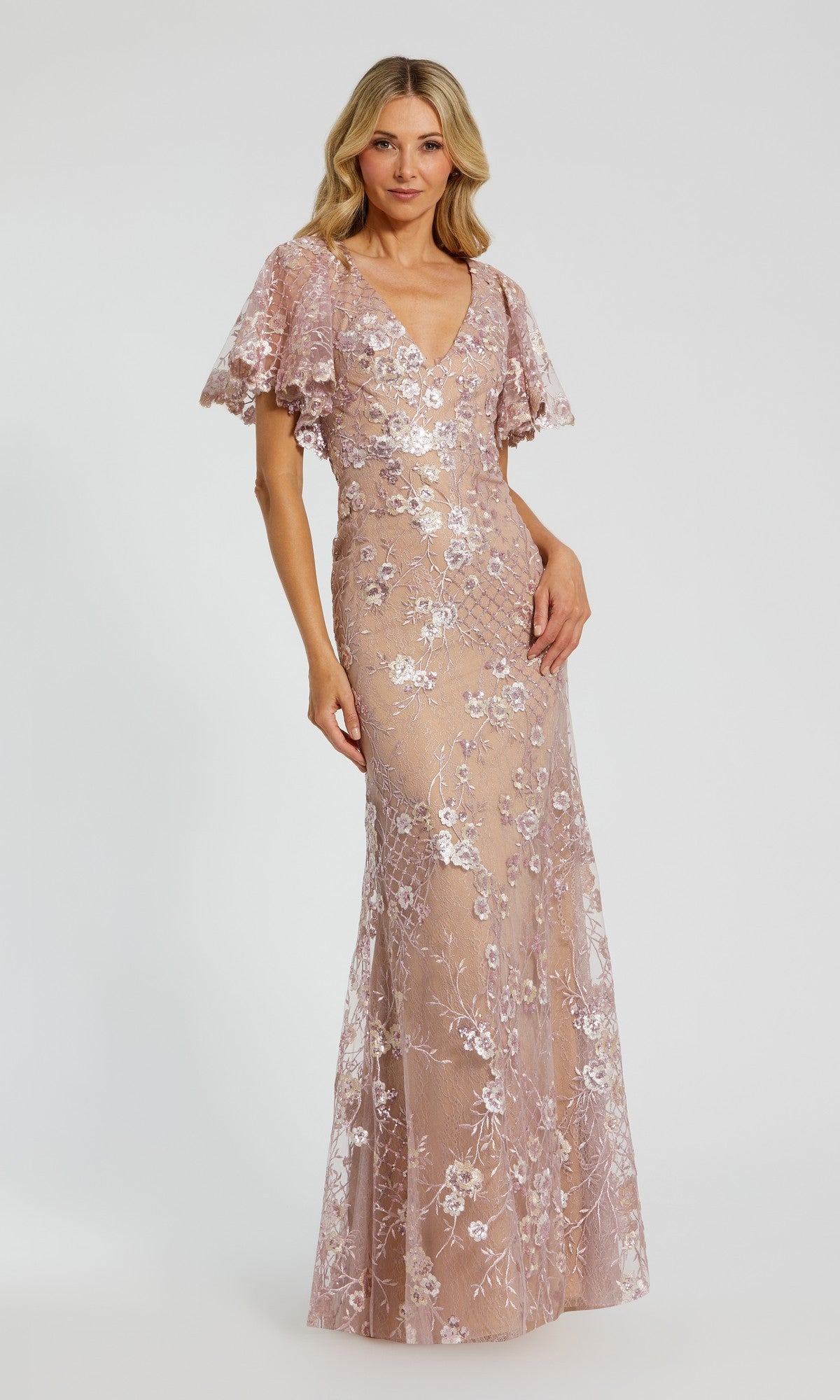 A woman models the Mac Duggal 68743 long formal dress in rose pink, featuring short flutter sleeves and floral embroidery, set against a plain background.